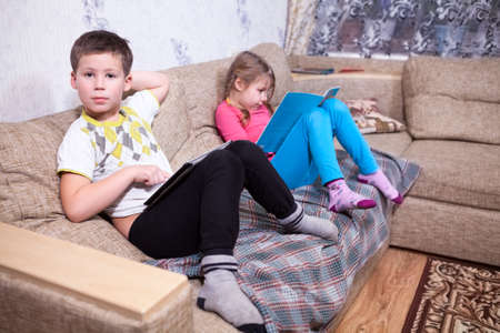 Boy with electronic device and girl with paper book in domestic roomの写真素材