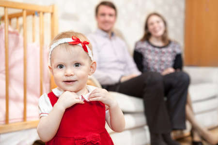 One year old baby in red dress with parents are on backgroundの写真素材