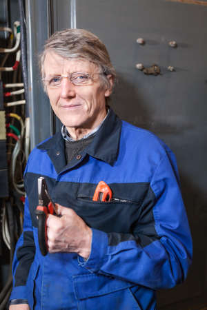 Mature electrician with pliers in his hands standing near high voltage boxの写真素材