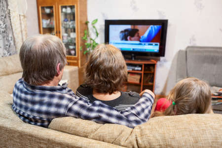 Caucasian father, mother and daughter sitting on the couch and watching tv set