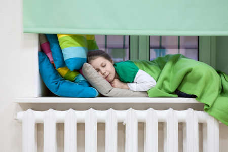 Caucasian child sleeping in clothes on the windowsillの写真素材