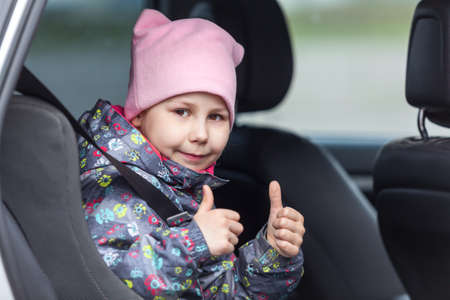 Little child is in the booster chair fastening with car seatbelt, thumbs up showingの写真素材
