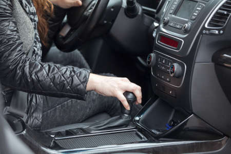 Caucasian female hand holding levels of automatic car gearbox, driver seat close-up viewの写真素材