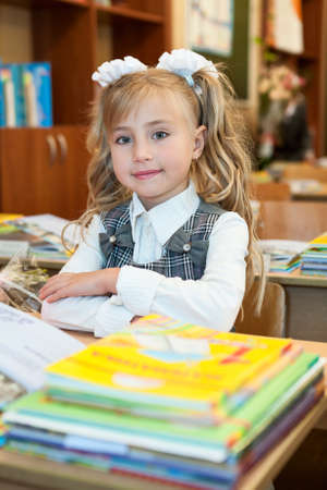 First-form schoolgirl sitting at school desk at lesson in classroom, looking at cameraの写真素材