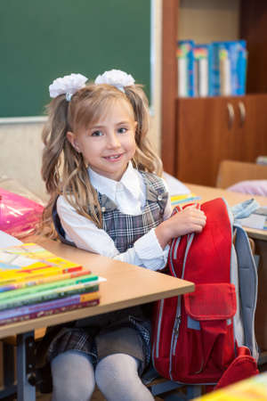 Schoolgirl in uniform sitting at desk and getting out things of bagの写真素材