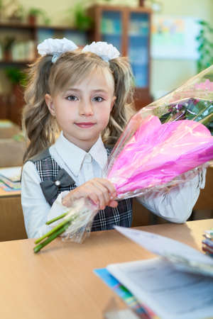 Happy schoolgirl holding hands bouquet of flowers sitting at the school deskの写真素材