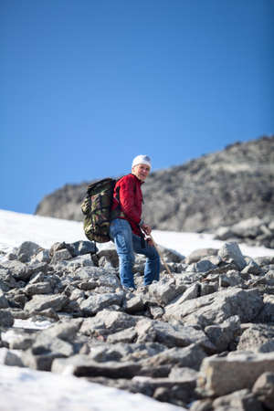 Mature Caucasian hiker in red jacket standing on the top of mountain at steep stony slopeの写真素材