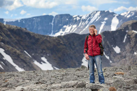 Senior Caucasian hiker with a backpack talking on cellphone in the mountains, copy spaceの写真素材