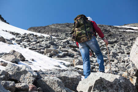 Rear view of hiker climbing on steep stony slope in mountainsの写真素材