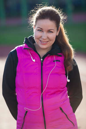 Smiling Caucasian young woman portrait, standing at the stadium in sportive clothes