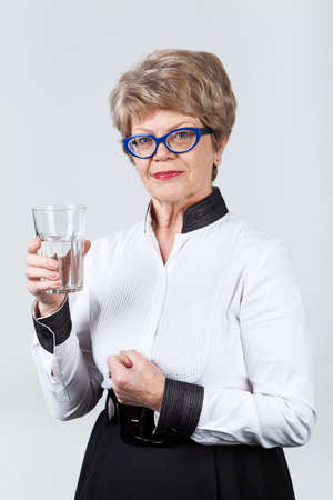 Elderly Caucasian woman holding hand glass with clear water and clenching first of other handの写真素材