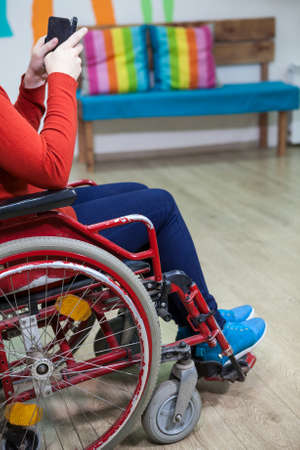 Unrecognizable Caucasian disabled woman sitting wheel-chair and watchin message with smartphone, indoorの写真素材