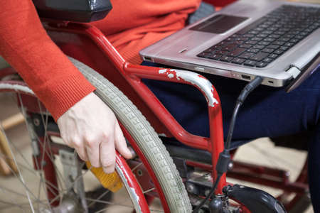 Invalid wheel-chair with sitting disabled person and laptop on kneesの写真素材