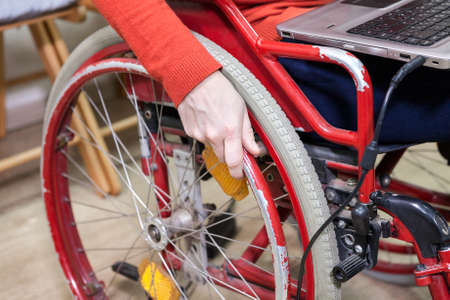 Hand of Caucasian disabled woman holding wheel, opened laptop laying on the kneesの写真素材