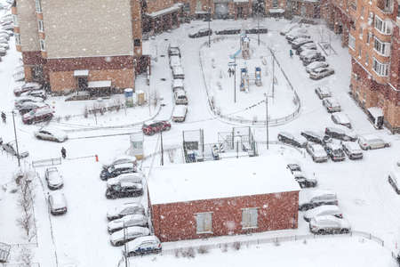 Strong snowfall is in apartment building inner yard, cars parking under snow, winter seasonの写真素材