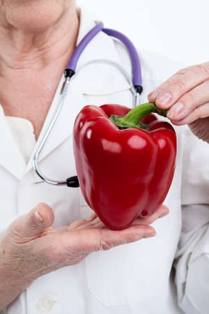 Large red bell pepper in form of heart in the hands of doctor, isolated on white background