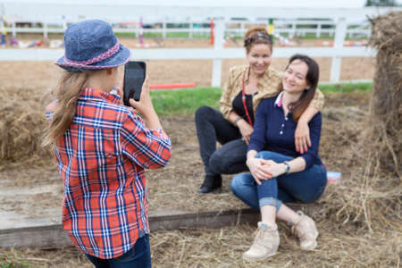 Small girl photographing of two women sitting next to the hay on cellphoneの写真素材