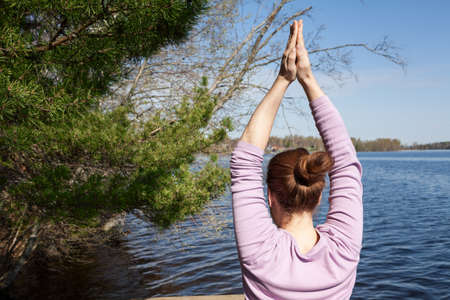 Rear view of young woman doing yoga exercises on lake shoreの写真素材