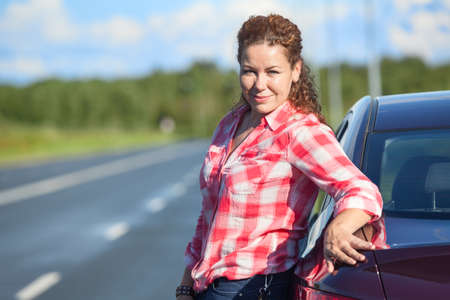 Portrait of curly hair attractive woman in red shirt leaning her car, copy space