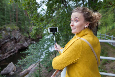 Pretty woman holding smartphone on selfie stick and looking at camera