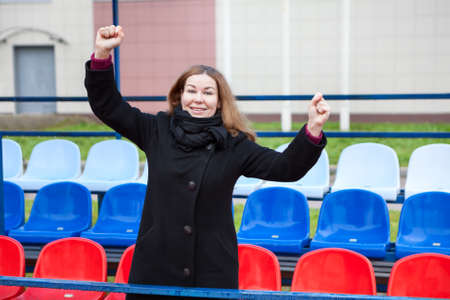 Female fan in black coat cheers on the team on national colors stadium seatsの写真素材