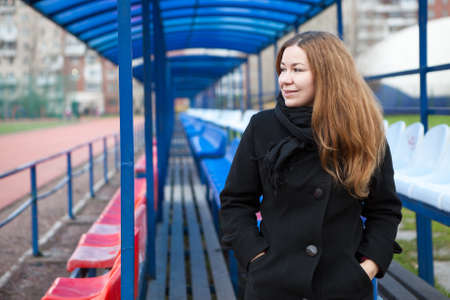 Young woman in a black coat sitting on an empty grandstand outdoor stadium and looking awayの写真素材
