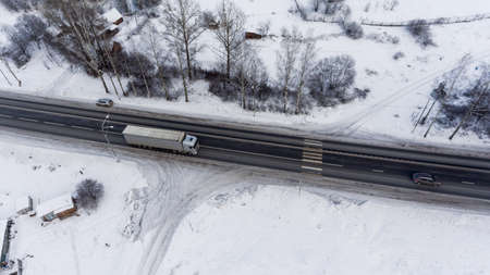 Freight semitrailer truck driving on the federal highway M10 at winter season. The Yazhelbitsy village, Novgorod district. Russia. Aerial viewの写真素材