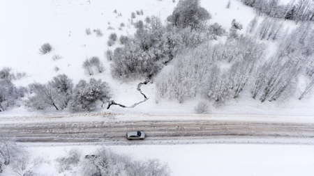 Aerial view at the suv driving on icy country winter road in white fields