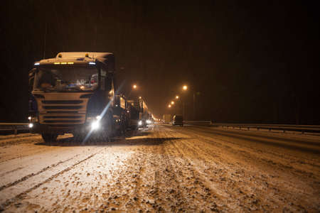 Long traffic jam is on wintry federal road M10 at evening time. Semitrailers standing to Moscow direction due road accident. Snowfall. Russiaの写真素材