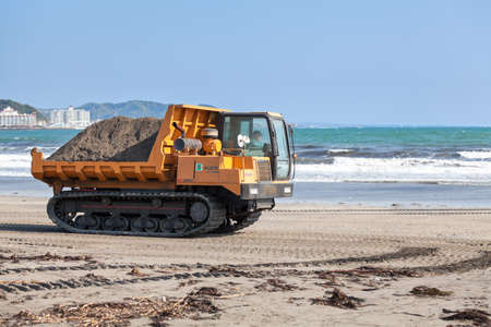 KAMAKURA, JAPAN - CIRCA APR, 2013: Crawler transporter full of sand drives on sandy beach on coast...