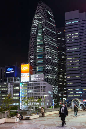 TOKYO, JAPAN - CIRCA APR, 2013: Building of Mode Gakuen Cocoon Tower is in the Nishi-Shinjuku district in Shinjuku at night time. People walk on footbridge from metro stationのeditorial素材
