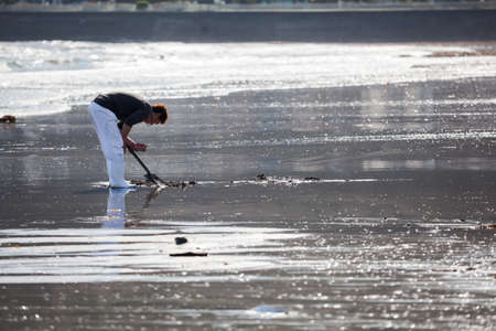 KAMAKURA, JAPAN - CIRCA APR, 2013: Japanese young man collects sea food at the low water on sandbank in Nagai beach. Low tide water is on coast of Pacific oceanのeditorial素材