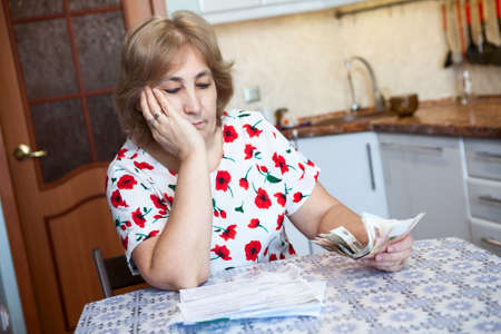 Caucasian woman looks with sad at receipts for communal payment while sitting on the kitchenの写真素材