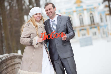 Happy young newly married couple holding in hands the Russian word love. Winter seasonの写真素材