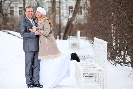 Young bride and groom on a walk in a winter park, standing next to a white iron benchの写真素材