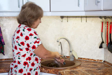Caucasian senior woman washing glass in kitchen sinkの写真素材