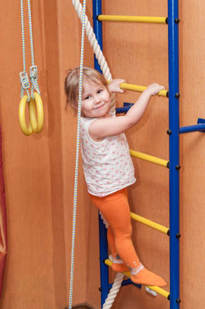 Little girl climbing wall-mounted ladder in domestic room