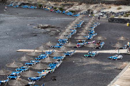 CALLAO SALVAJE, TENERIFE, CANARY, SPAIN-CIRCA JAN, 2016: Blue sunbeds and strawy parasols are on the Playa de Ajabo beach. Atlantic ocean. Public beach with black volcanic sand is on southwestのeditorial素材