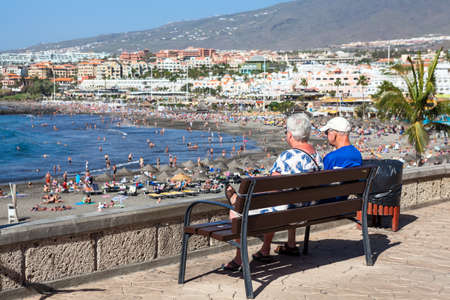 COSTA ADEJE, TENERIFE, SPAIN-CIRCA JAN, 2016: European senior couple rest on the bench with view at the sandy beach the Torviskas. Torviscas and Fanabe are city resorts with grey sandのeditorial素材