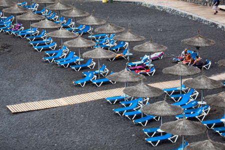 CALLAO SALVAJE, TENERIFE, CANARY, SPAIN-CIRCA JAN, 2016: Blue sunbeds and straw parasols are on the Playa de Ajabo beach. Atlantic ocean. Small public beach with black volcanic sand is on southwestのeditorial素材