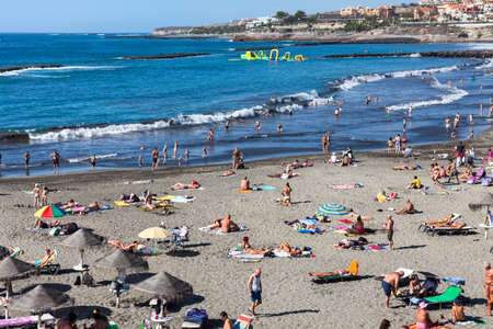 COSTA ADEJE, TENERIFE, SPAIN-CIRCA 2016, JAN: People sunbathe and swim on the grey Blue Flag beach of the Playa Torviscas. South of Tenerife island. The Playa Torviscas is the biggest city beachのeditorial素材