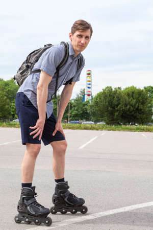 Caucasian man in roller-skates with backpack standing on asphalt road, full-lenght portraitの写真素材