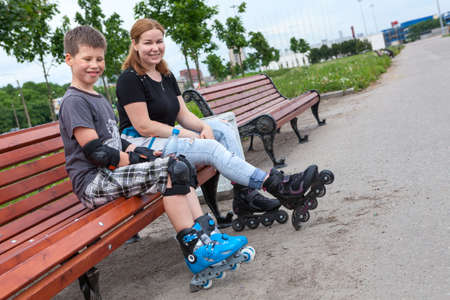 Caucasian young boy in roller-skating equipment and a mom are skating on city streets
