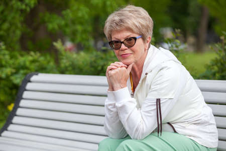 Caucasian woman pensioner sits and rests on a bench while walking in a park, copyspaceの写真素材