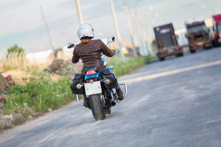Woman motorcyclist wearing leather jacket driving on asphalt highway, rear viewの写真素材