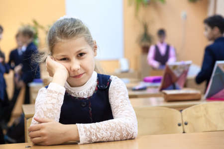 Young girl a pupil is in a bad temper on recess while other children playing on backgroundの写真素材