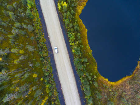 Passenger car driving top-soil road among swamp and small lakes, Karelia, north of Russiaの写真素材