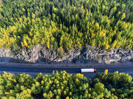 Top view at white semitrailer truck driving between rock tunnel in autumn forest of Karelia, Russiaの写真素材