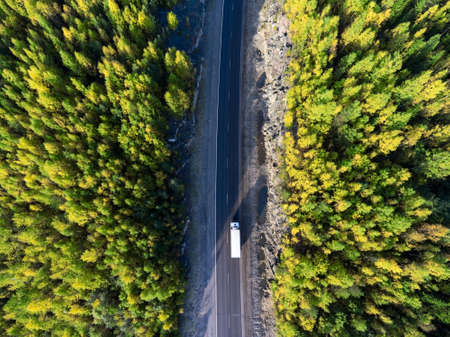 Top view at white freight truck driving between rock tunnel in golden autumn forest of Karelia, Russiaの写真素材