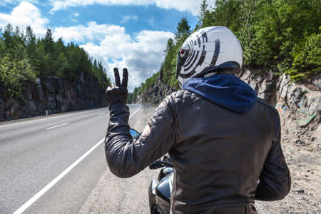 Motorcycle driver rear view at the asphalt road, sitting on motorbike and showing victory sign wit handの写真素材